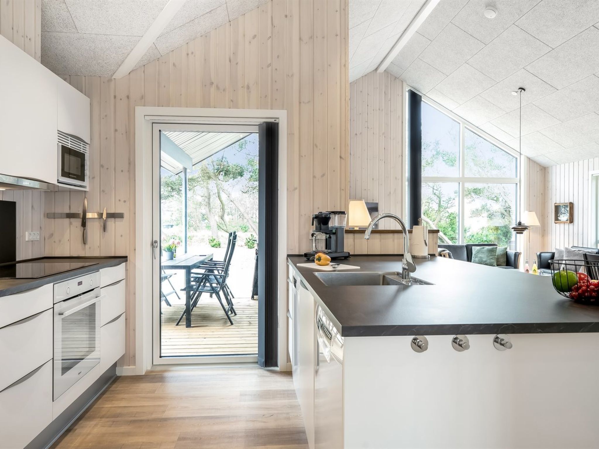 A modern kitchen with a large island, a dining area with outdoor seating, and a view of the outdoors.