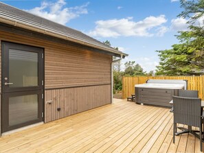 A wooden deck with a hot tub and chairs, a sliding glass door, and a fenced backyard.