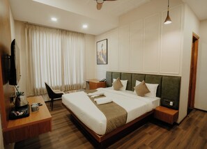 Habitación de hotel con cama, mesitas de noche, escritorio con silla, televisor y ventana con cortinas.