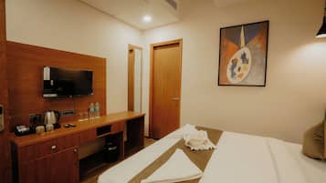 A hotel room with a wooden desk, a television, a painting, and a bed with a quilted bedspread.