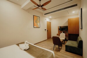Habitación de hotel con cama, escritorio, silla, sofá, televisión y ventilador de techo.