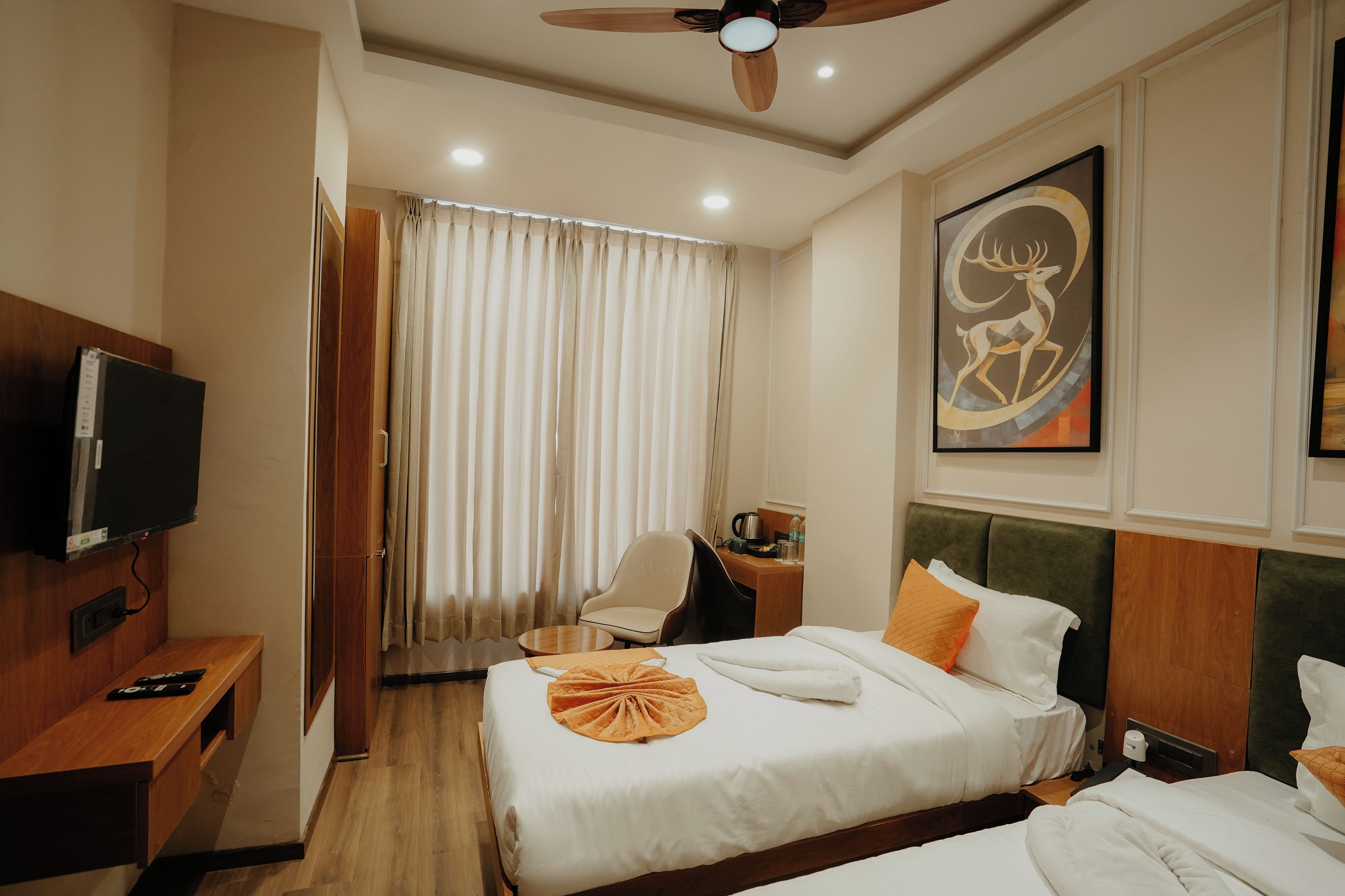 Habitación de hotel con cama, escritorio, silla, televisor, ventilador de techo y una pintura.