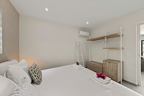 Ein modernes Schlafzimmer mit einem großen Bett, einer Holzkommode, einer Strickleiter und einer weißen Klimaanlage an der Wand.