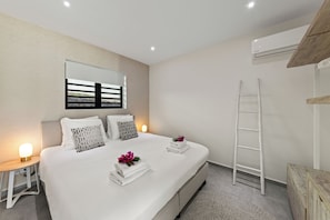 A modern bedroom with a large bed, bedside lamps, a ladder, and a wooden cabinet. - Apartment Ayana Mambo Beach (Willemstad)