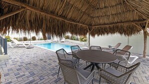 Une terrasse ext érieure dotée d’un toit de chaume, d’une piscine et de mobilier en osier.