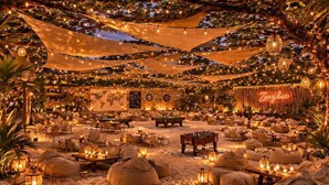 An outdoor lounge area with tables, chairs, and a foosball table, decorated with string lights and lanterns. - White House social club  (Paje)