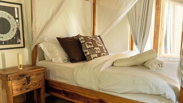 A wooden bed with a canopy, a nightstand with a drawer, and a framed picture on the wall. - White House social club  (Paje)