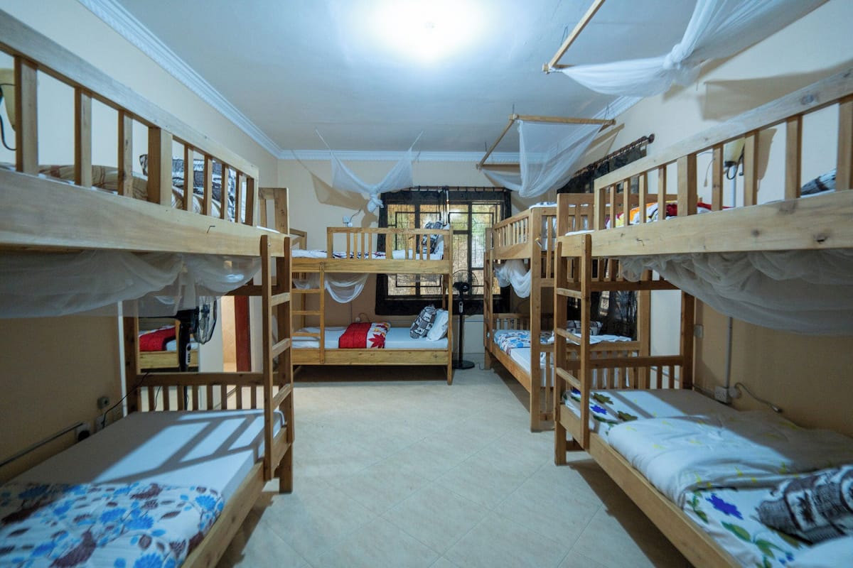 A dormitory room with bunk beds, a window with curtains, and a bed with a floral bedspread.