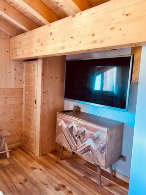 A wooden cabin interior with a large TV mounted on a wall, a wooden cabinet with a mountain design, and a wooden floor. - Ciméro Duplex Chalet—Luxury, Spa, Accommodates 10 Guests (Formiguères)