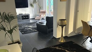 A modern living room with a dining area, a TV mounted on the wall, and a large window providing natural light. - Beautiful vacation rental with a terrace (Mülheim-Kärlich)