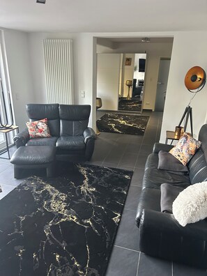 A modern living room with a black leather sofa, a black and gold rug, and a white fluffy throw.