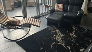 A modern living room with a black leather sofa, a black and gold rug, and a glass door leading to an outdoor patio. - Beautiful vacation rental with a terrace (Mülheim-Kärlich)