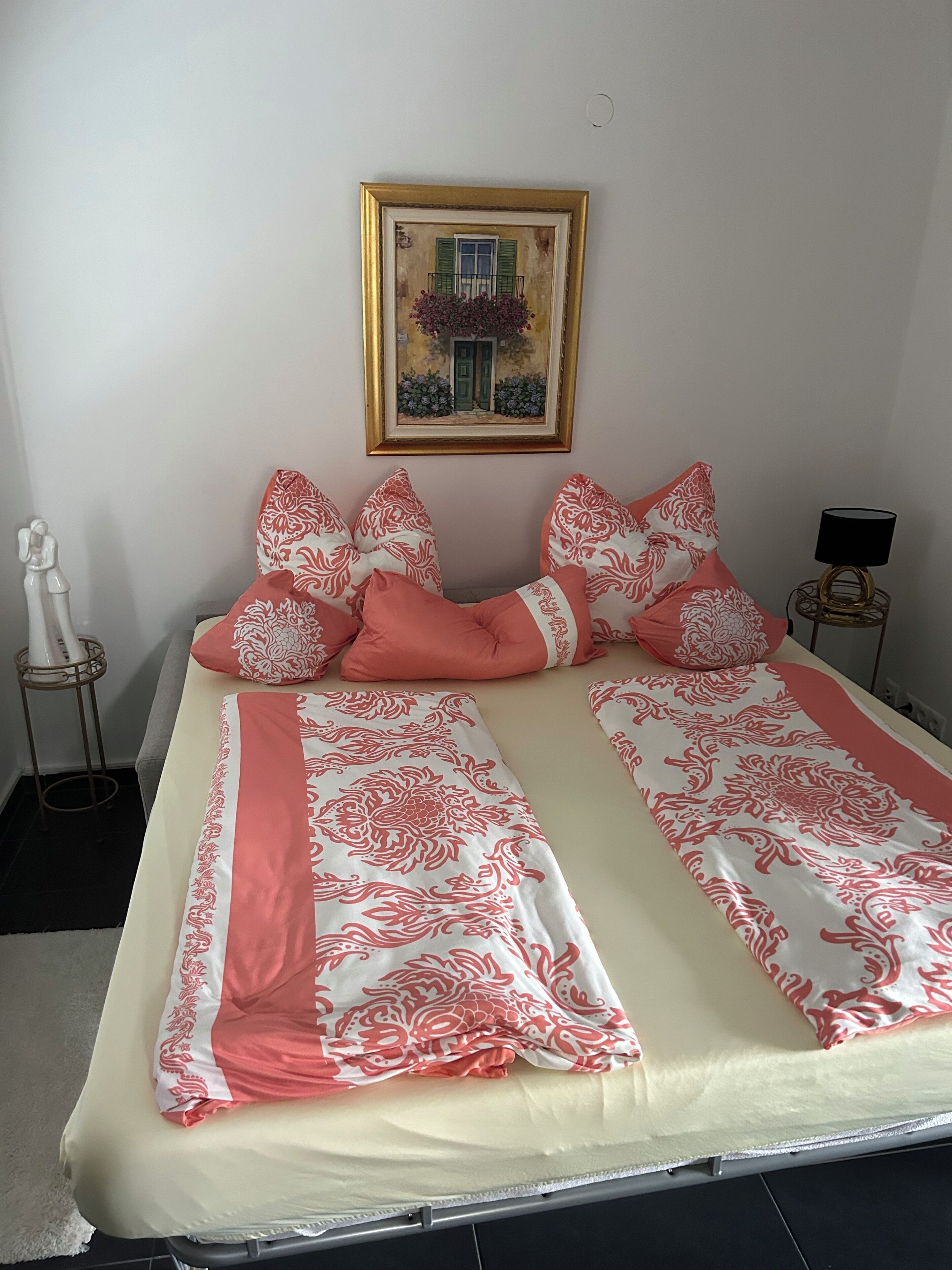 A bed with a patterned bedspread, pillows, a bedside table with a lamp, and a framed picture on the wall.