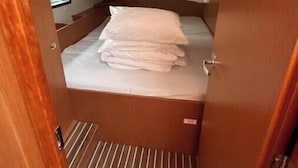 Une petite cabine avec un lit simple, un sol à rayures, une petite fenêtre et une porte donnant sur une autre pièce.