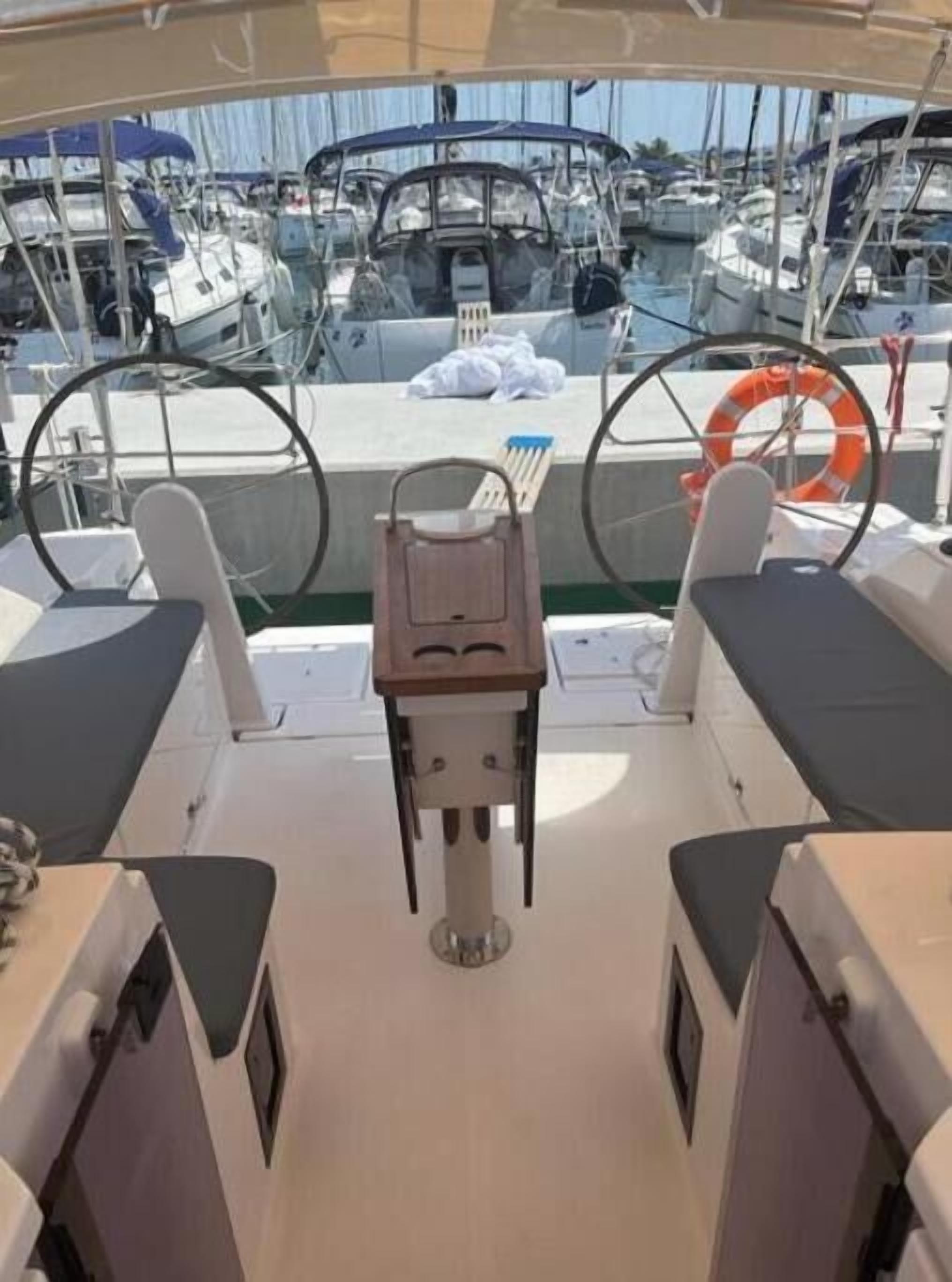 Cubierta de barco con una mesa central, dos asientos acolchados, un timón y un flotador salvavidas.