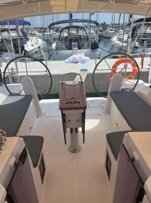 A boat deck with a central table, two cushioned seats, a steering wheel, and a life ring.