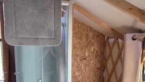 A room with a glass shower enclosure, wooden flooring, and a window with a curtain. - Unique, fully equipped yurt for 2 people (Querrien)