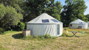 A yurt with a door, a small wooden structure, and two chairs in a grassy area with trees in the background. - Unique, fully equipped yurt for 2 people (Querrien)