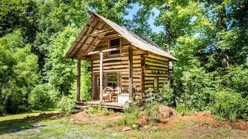 Una cabaña rústica de troncos con un porche y una chimenea, rodeada de un denso bosque.