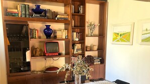 A dining area with a table, chairs, a vase with flowers, a bookshelf, and a television. - The Rose Apartment - Bologna (Bologna)