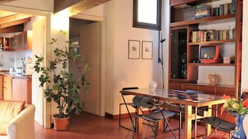 Un coin repas avec une table en bois, des chaises, une plante en pot et une bibliothèque contenant des livres et un téléviseur.