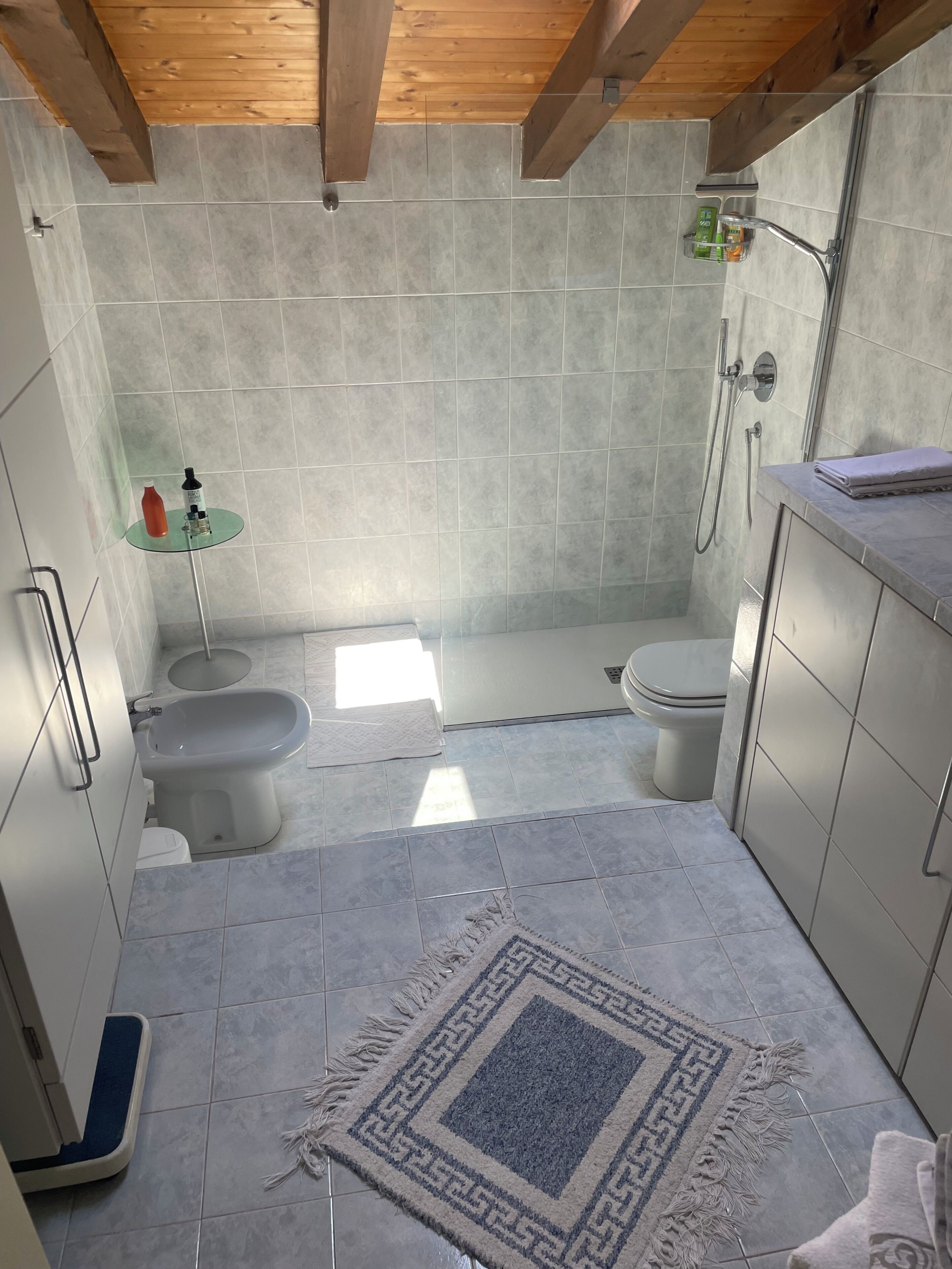 A bathroom with a shower, toilet, bidet, and a small glass table with toiletries.