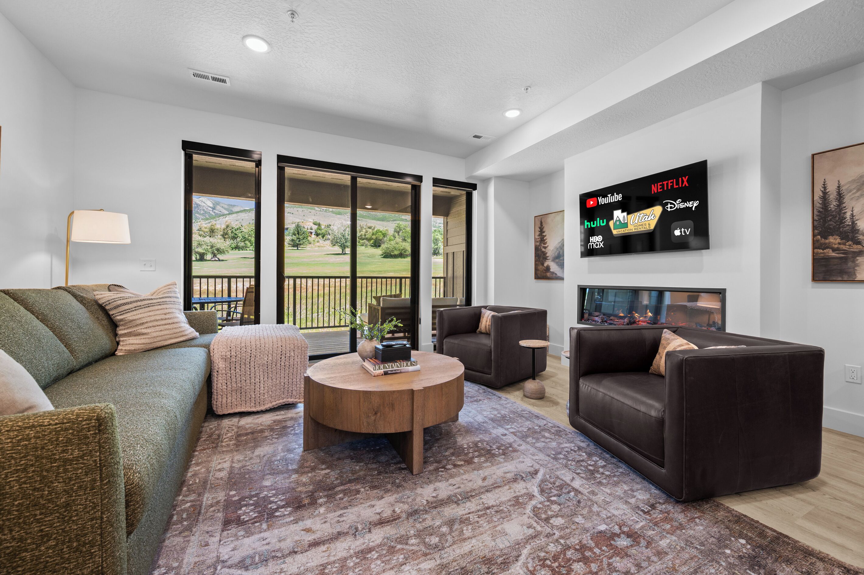A living room with a large flat-screen TV displaying streaming services, a green sofa, a brown leather couch, and a round coffee table.