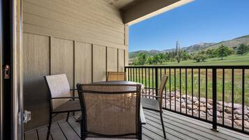 A covered outdoor area with a table and chairs, a view of a green landscape with trees and hills.