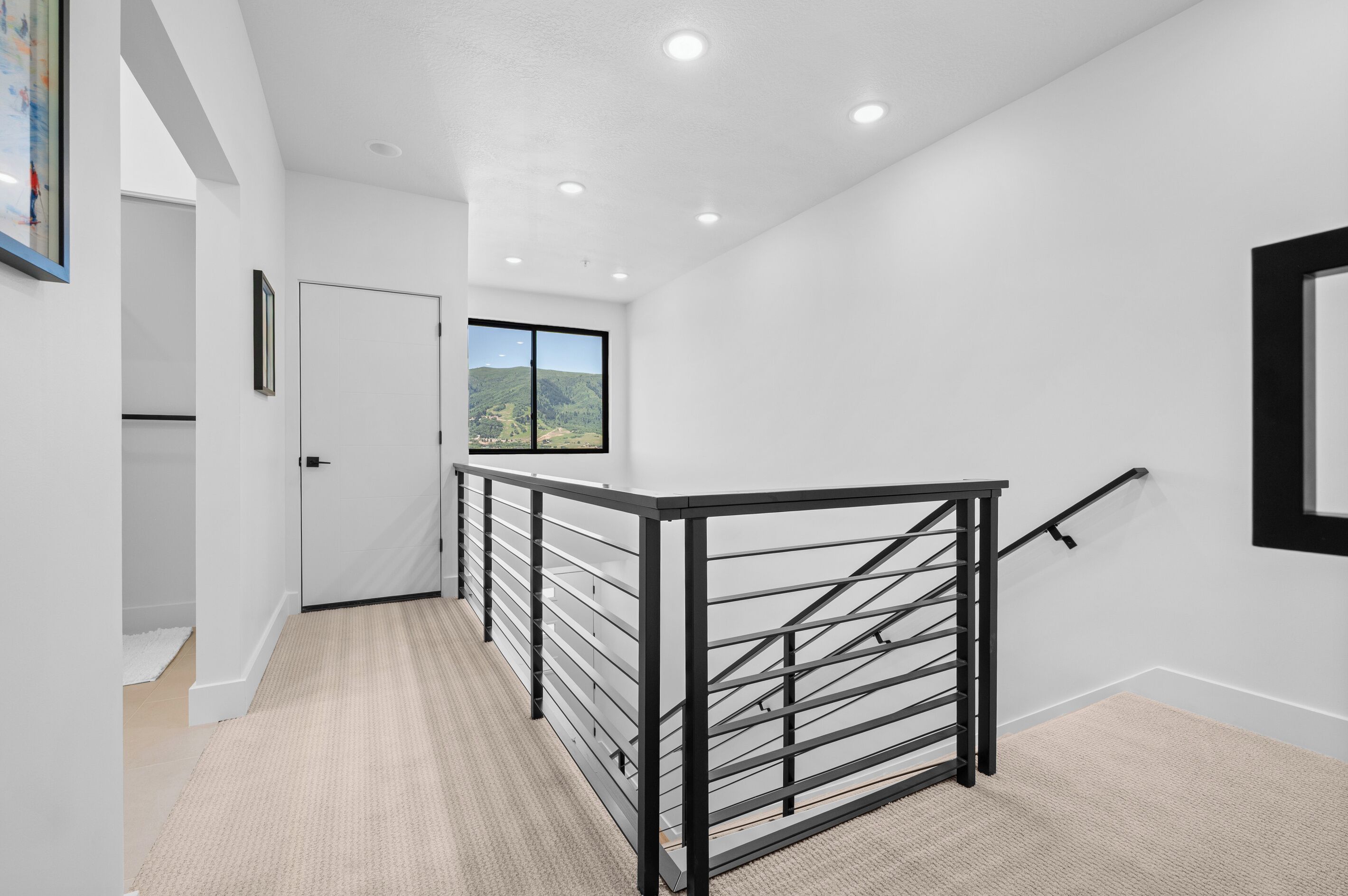 A modern interior with a staircase, white walls, and a view of a mountainous landscape.