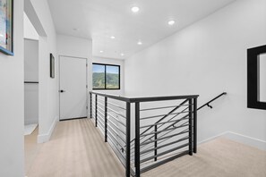Un interior moderno con una escalera, paredes blancas y vistas a un paisaje montañoso.