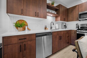 Una cocina moderna con gabinetes de madera, lavavajillas de acero inoxidable, microondas y cafetera.