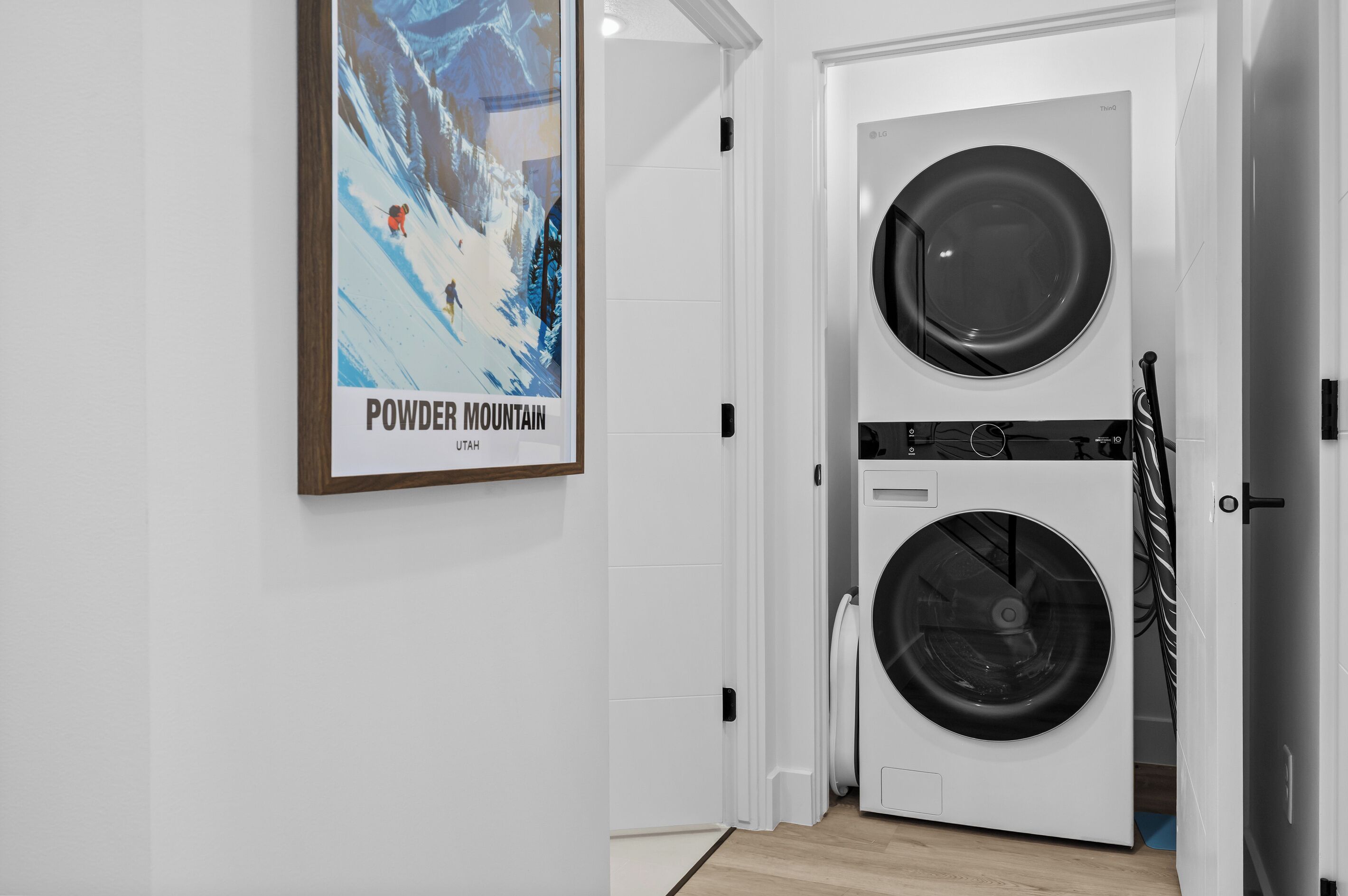 Une buanderie équipée d’un lave-linge et d’un sèche-linge à deux tambours, d’une affiche encadrée accrochée au mur et d’une porte blanche.