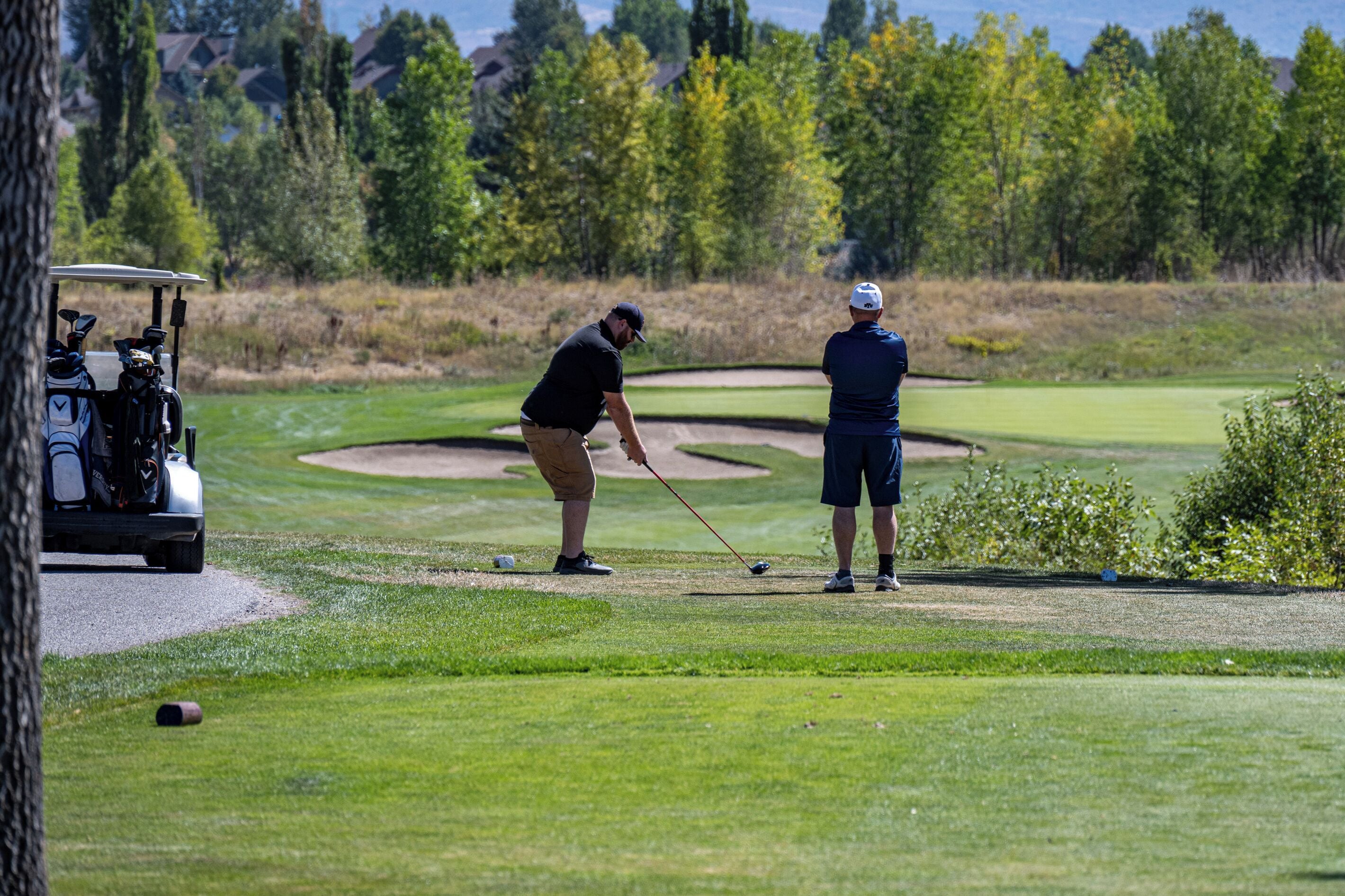 A golf course with a golf cart, a putting green, and a sand bunker.