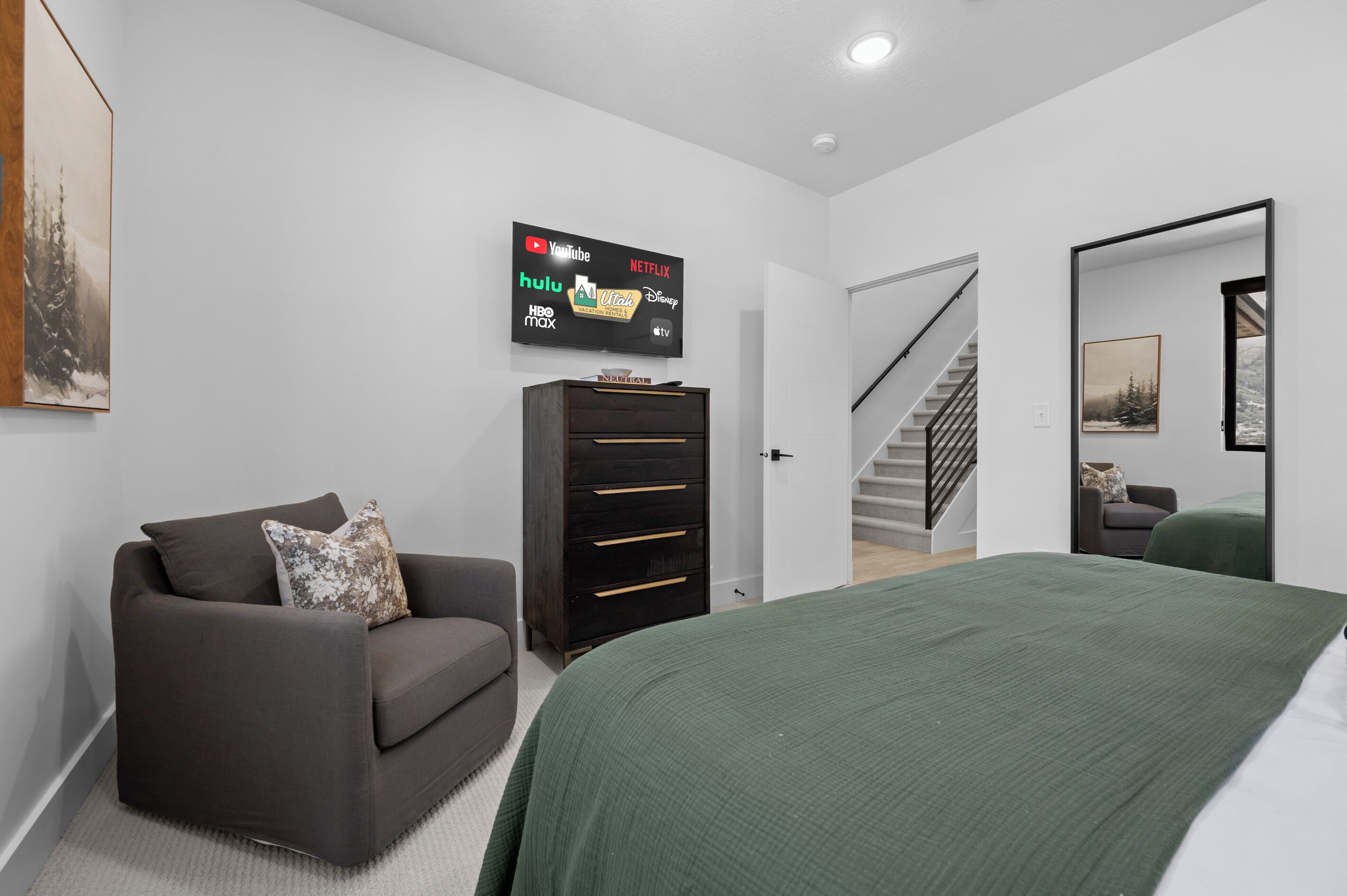 Une chambre moderne avec un lit, un canapé, un téléviseur fixé au mur et un escalier menant à une autre pièce.