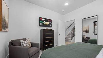 Une chambre moderne avec un lit, un canapé, un téléviseur fixé au mur et un escalier menant à une autre pièce.