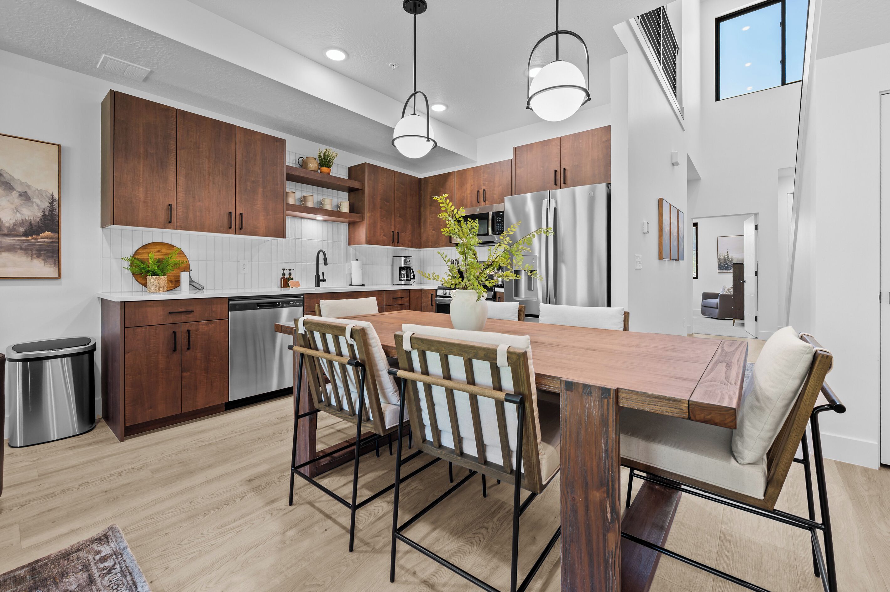 A modern kitchen with wooden cabinets, a stainless steel refrigerator, and a dining area with a wooden table and chairs.