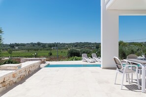 A poolside area with a view of a vineyard, stone walls, and outdoor furniture. - Charming Villa with Pool by Wonderful Italy (Ostuni)