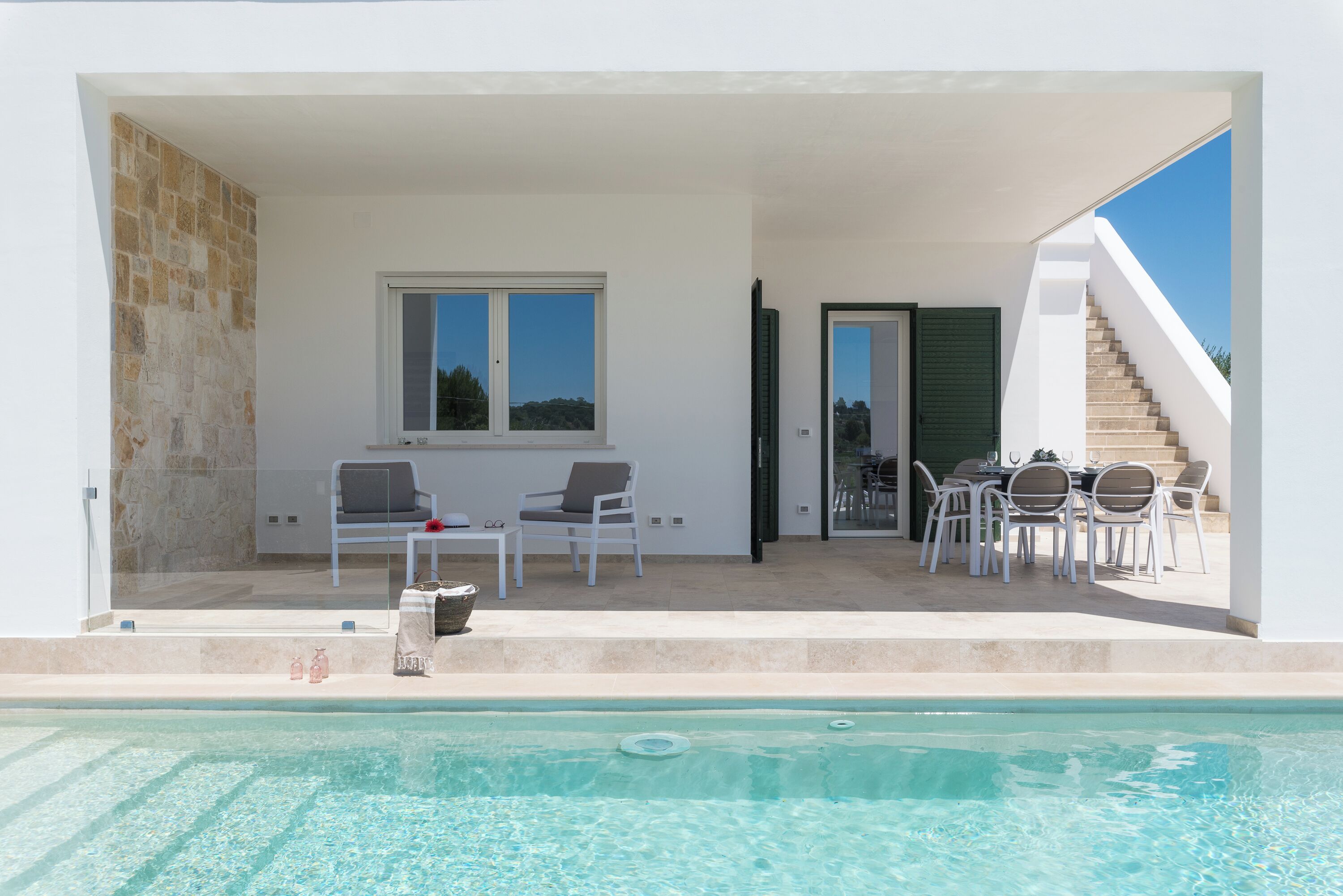A poolside area with a pool, two chairs, a table, and a staircase.