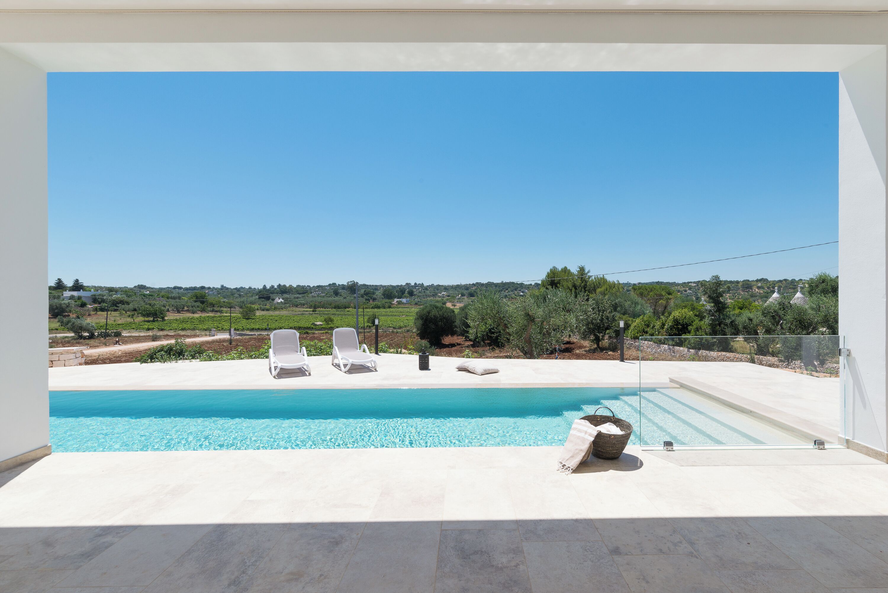 A pool with two white lounge chairs and a clear view of the countryside.