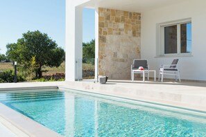 A swimming pool with a stone wall and two chairs. - Charming Villa with Pool by Wonderful Italy (Ostuni)