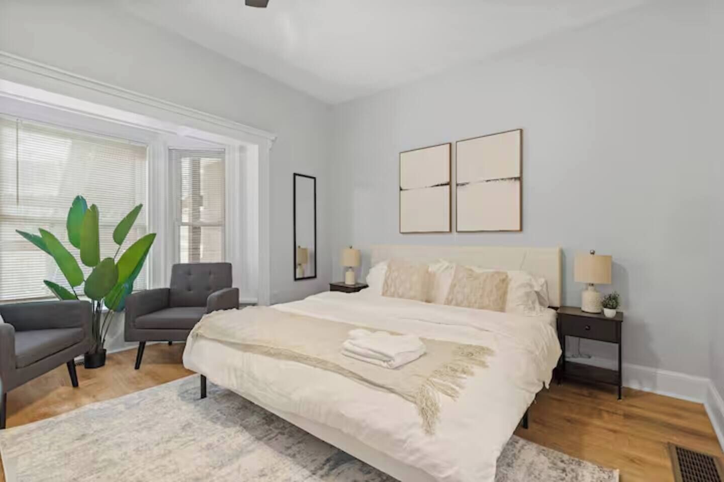 A bedroom with a large bed, two bedside tables, a chair, and a potted plant.