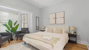 A bedroom with a large bed, two bedside tables, a chair, and a potted plant.