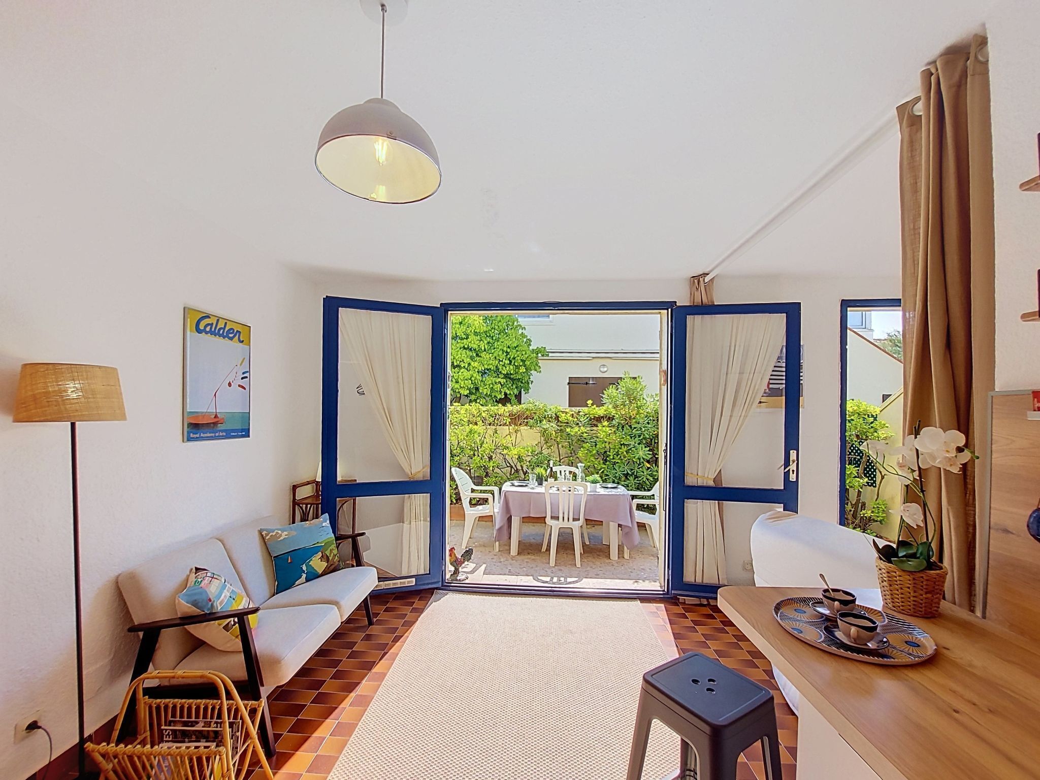 A room with a sofa, a small table, a lamp, and a view of an outdoor dining area.