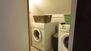 Een wasserette met twee wasmachines, een mand op de droger en een groene wasmand aan de muur.