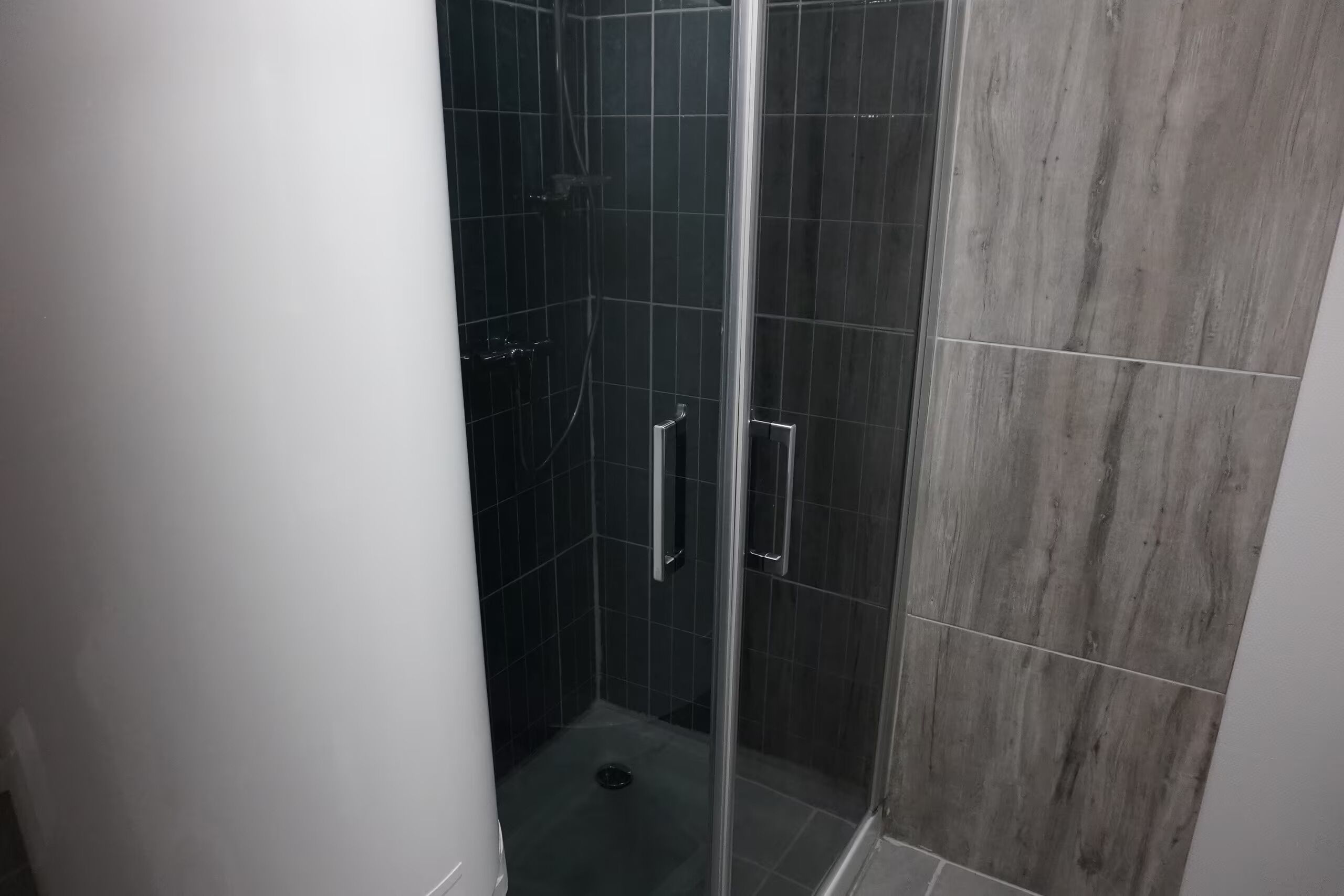 Eine Dusche mit Glastür, dunklen Fliesen und einer Metallgriff.
