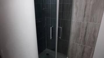 Eine Dusche mit Glastür, dunklen Fliesen und einer Metallgriff.