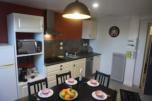 A compact kitchen with white cabinets, a microwave, a sink, and a dining table set with bowls and fruits.
