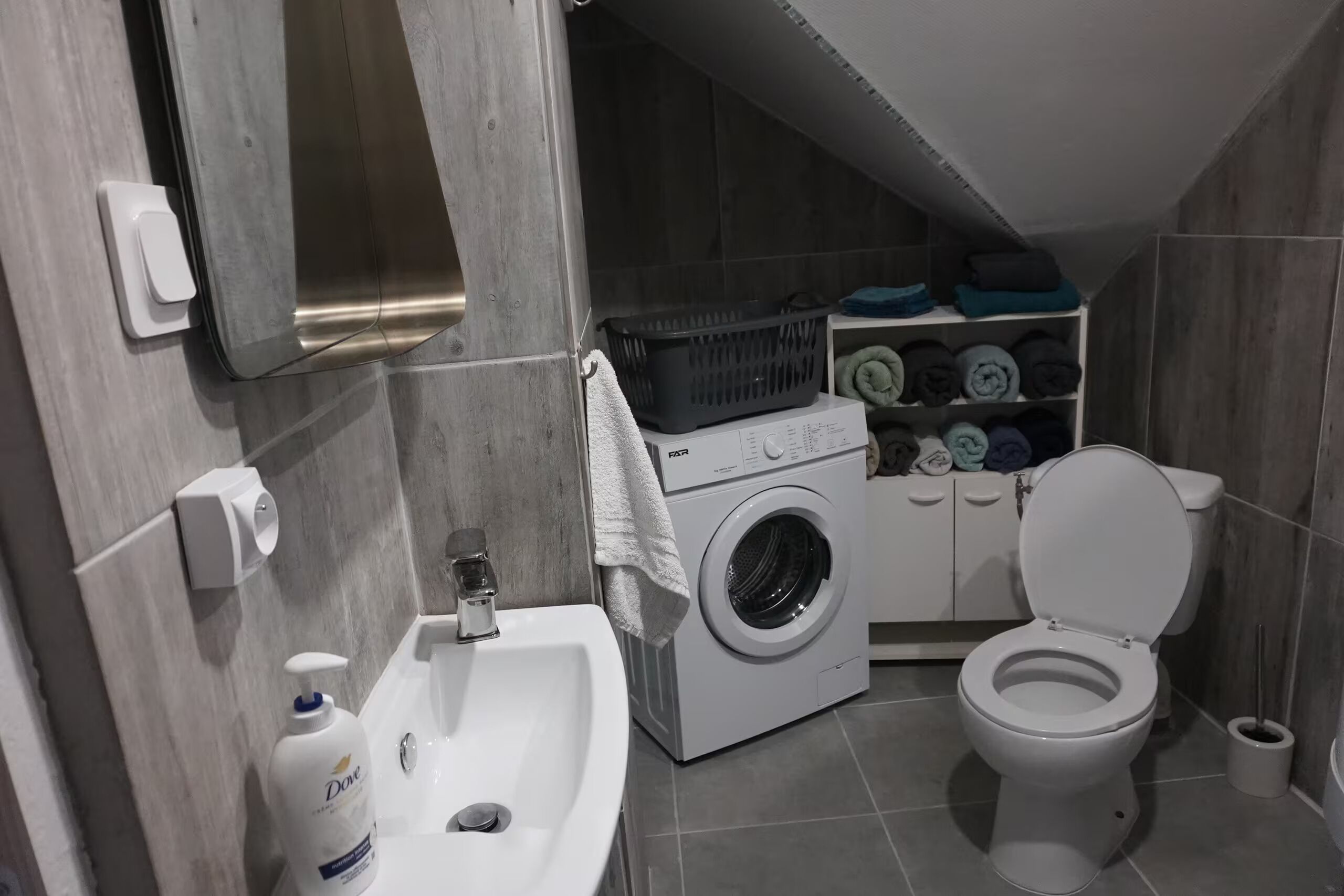 A compact bathroom with a sink, washing machine, and toilet.