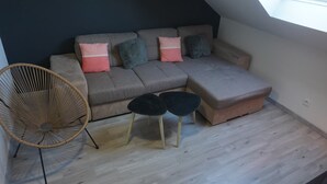 A cozy room with a sectional sofa, two small tables, a wicker chair, and a skylight. - Family-friendly city apartment with 2 free private indoor parking spaces (Beuvrages)