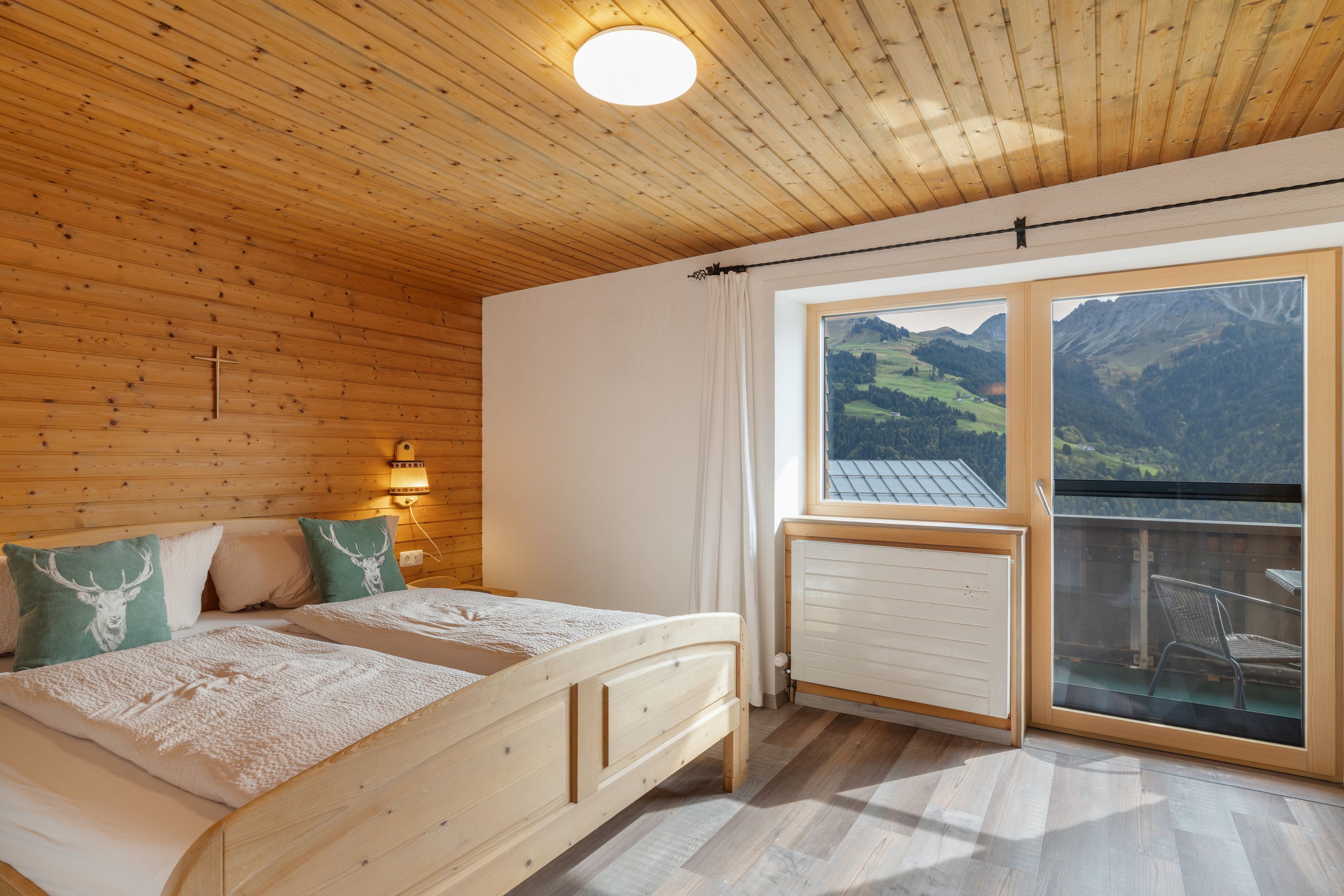 Une chambre avec un plafond en bois, un lit avec deux oreillers, une table de chevet avec une lampe et une fenêtre donnant sur les montagnes.